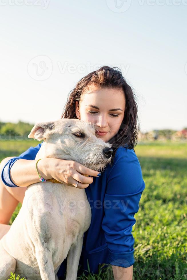 Hermosa joven sentada en la hierba abrazando a su perro en el parque foto