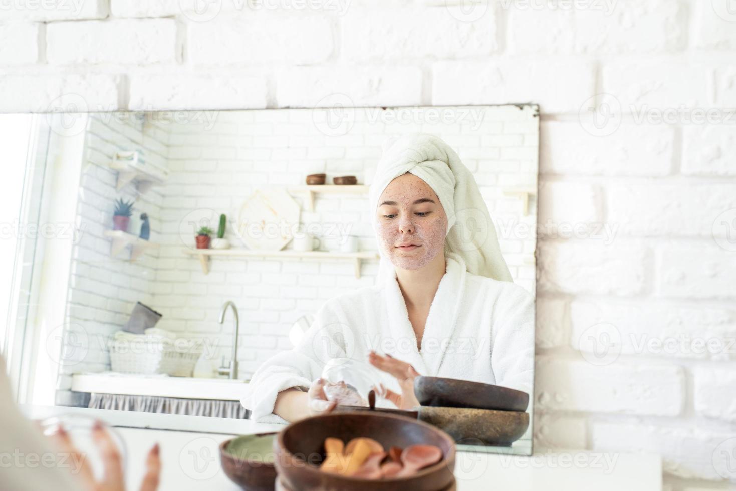 Feliz joven aplicando exfoliante facial en la cara foto