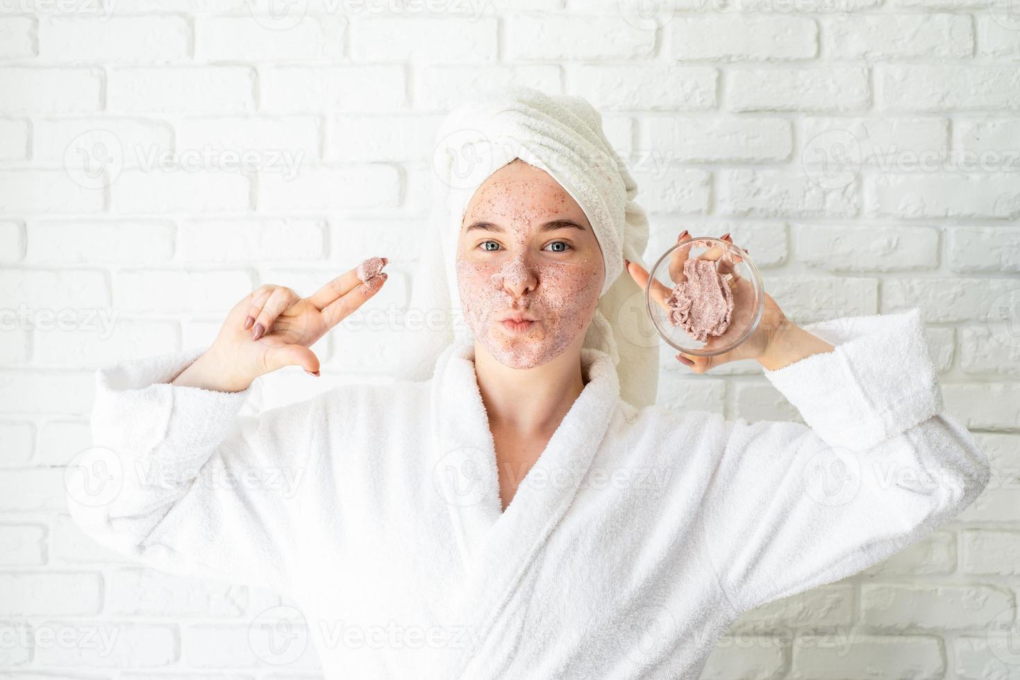 Feliz joven aplicando exfoliante facial en la cara foto