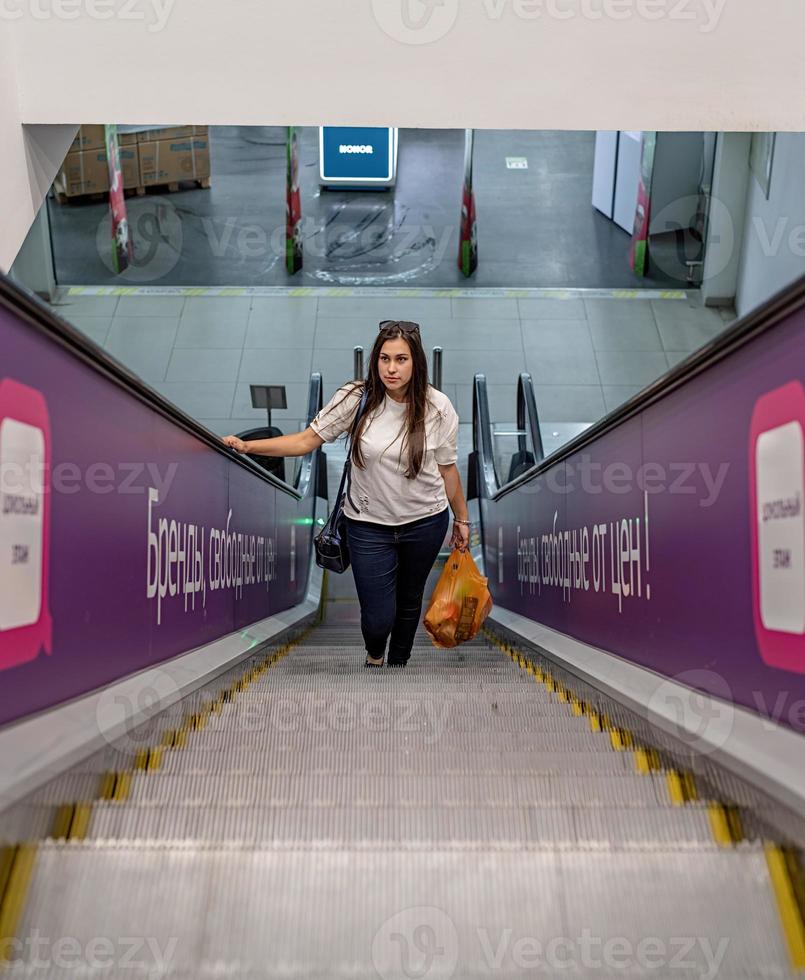 Young woman standing on escalator in shopping mall shopping photo