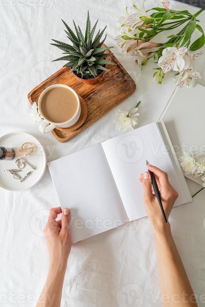 Opened book, coffee and flowers top view on white bed. Mock up design photo