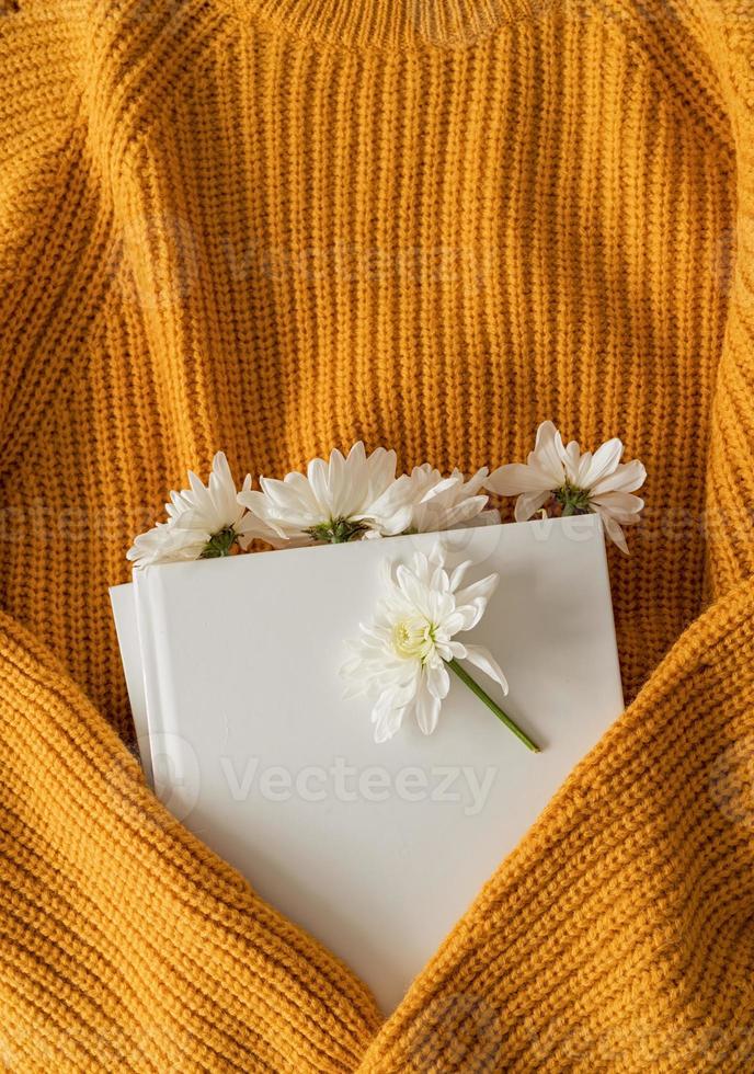 Top view of a book with white chrysanthemum flowers on yellow sweater photo