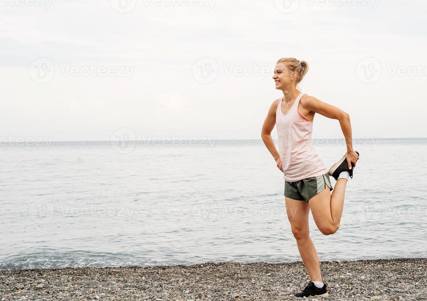 Blong athlete woman doing stretching exercises at the beach photo