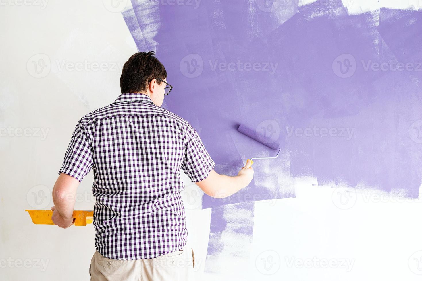 Man coloring wall with roller with purple paint photo