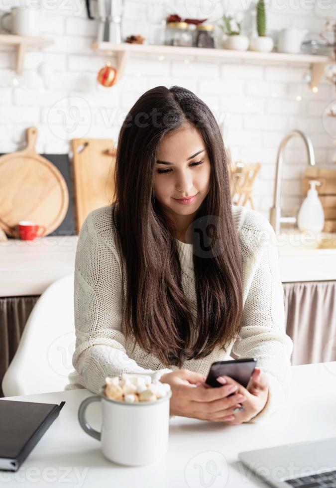 Mujer charlando con amigos usando su teléfono móvil en la cocina foto