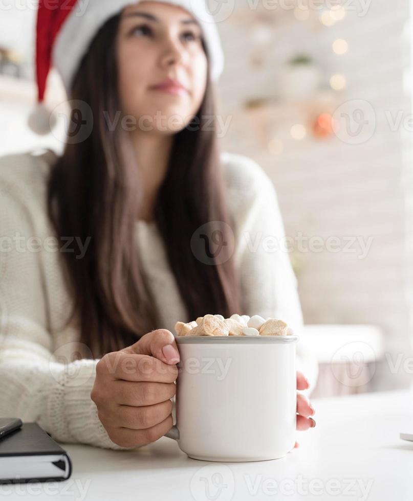 Brunette woman in santa hat holding a cup of marshmallow cocoa photo