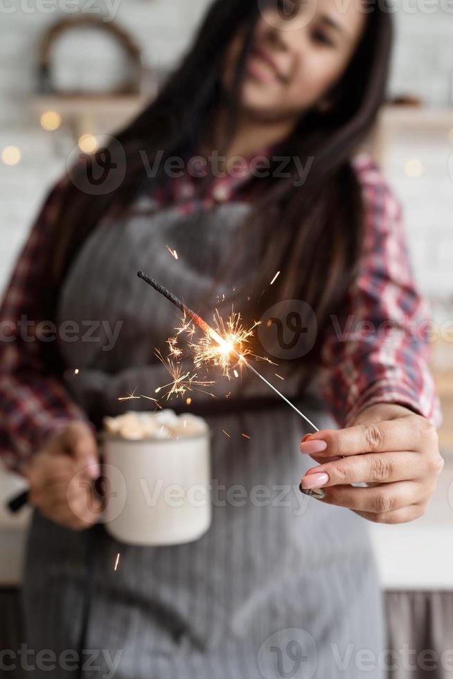 Woman with a cup of marshmallow cocoa and a sparkler photo