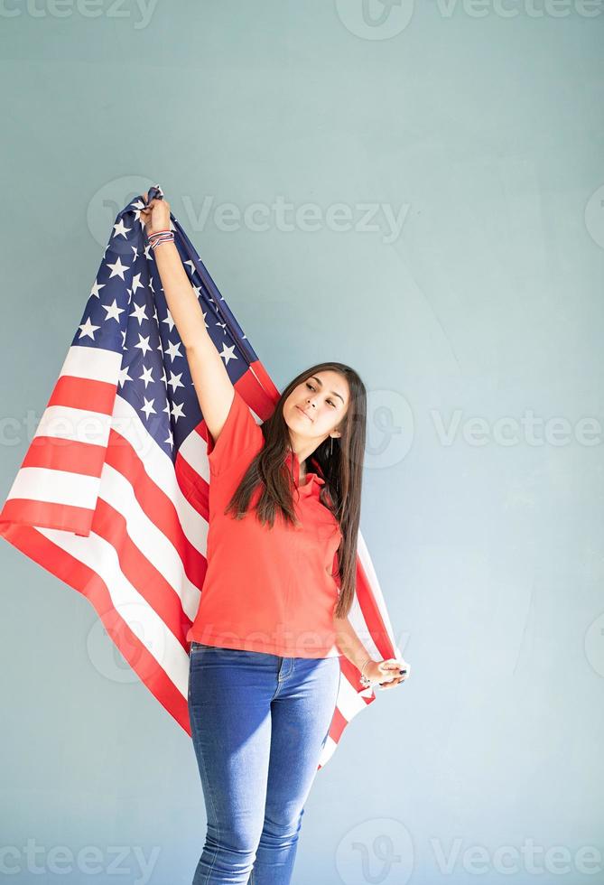 Beautiful young woman with American flag on blue background photo