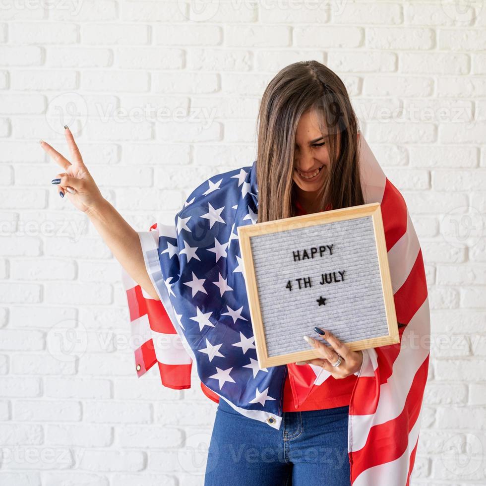 Mujer con bandera americana sosteniendo un tablero de letras con palabras feliz 4 de julio foto