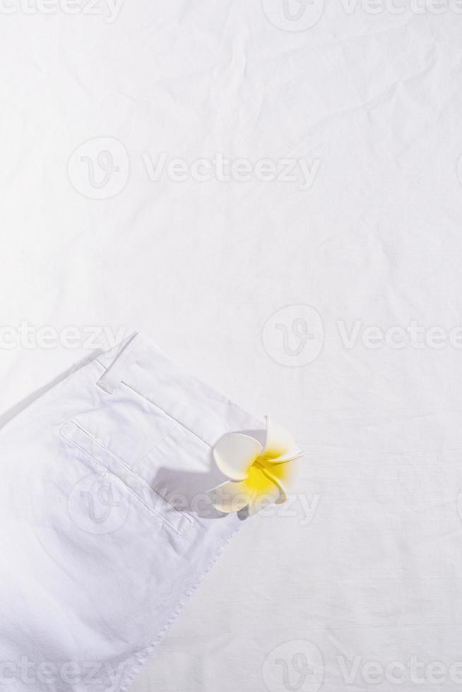 Pantalones vaqueros de verano blanco con flor de plumeria sobre fondo blanco. foto