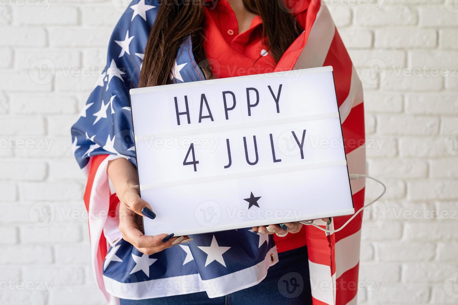 Mujer con bandera americana sosteniendo lightbox con palabras feliz 4 de julio foto