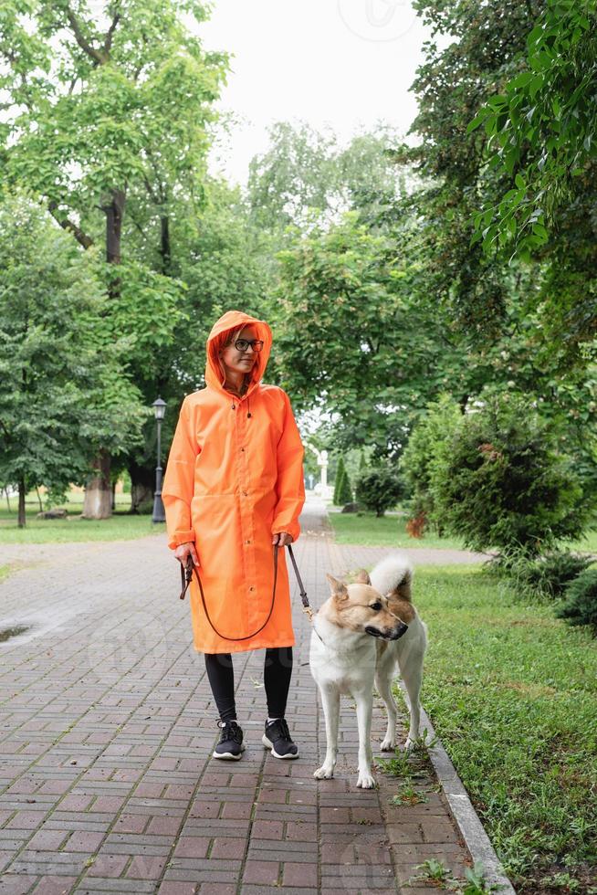 Mujer joven en impermeable naranja caminando con su perro en un parque foto