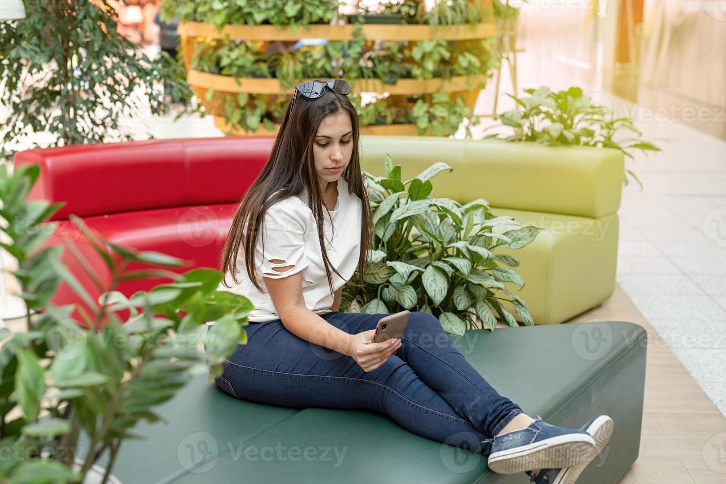 mujer sentada en el sofá en el centro comercial, mirando el teléfono foto