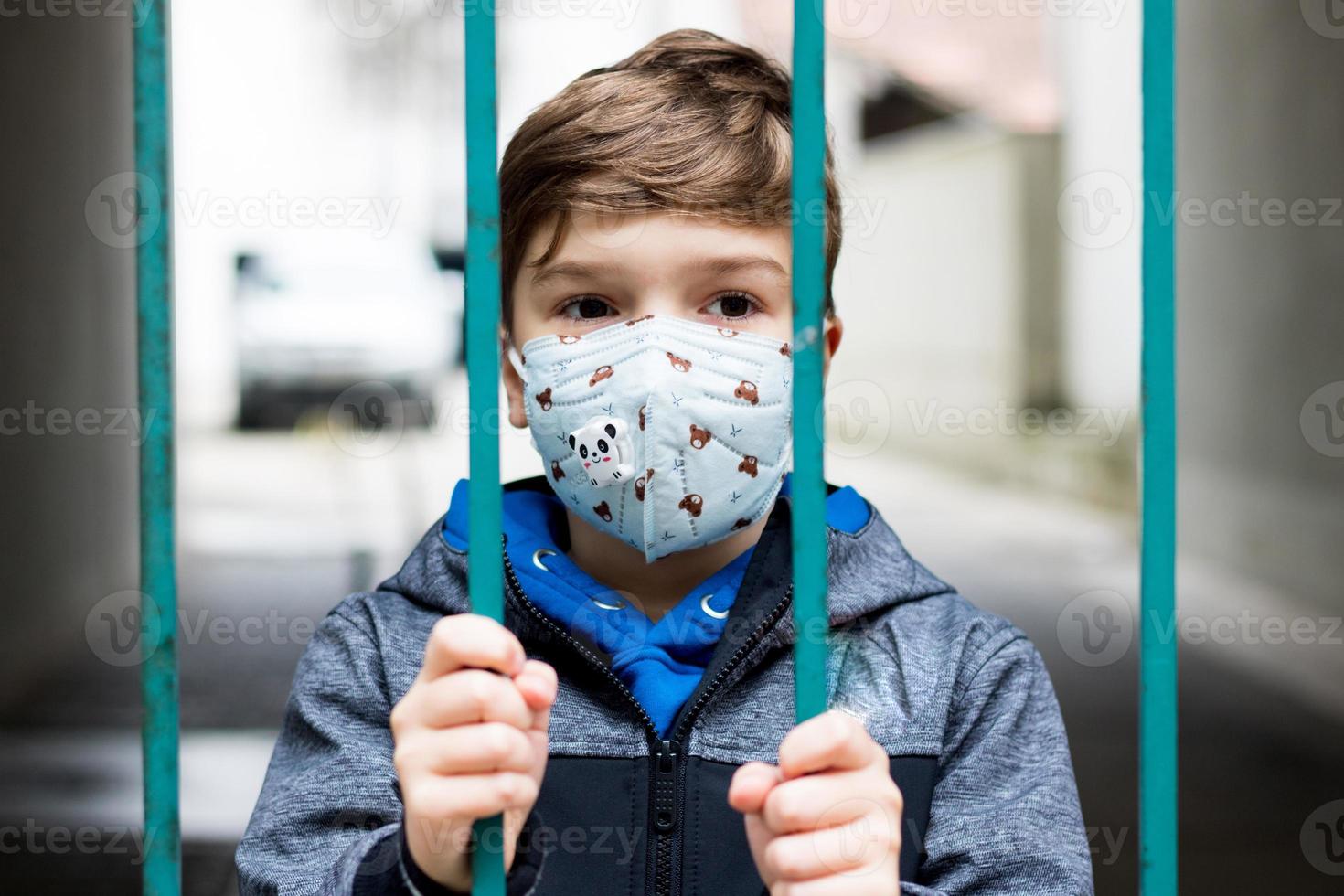 niño con mascarilla de pie detrás de la puerta durante el encierro del covid-19. foto