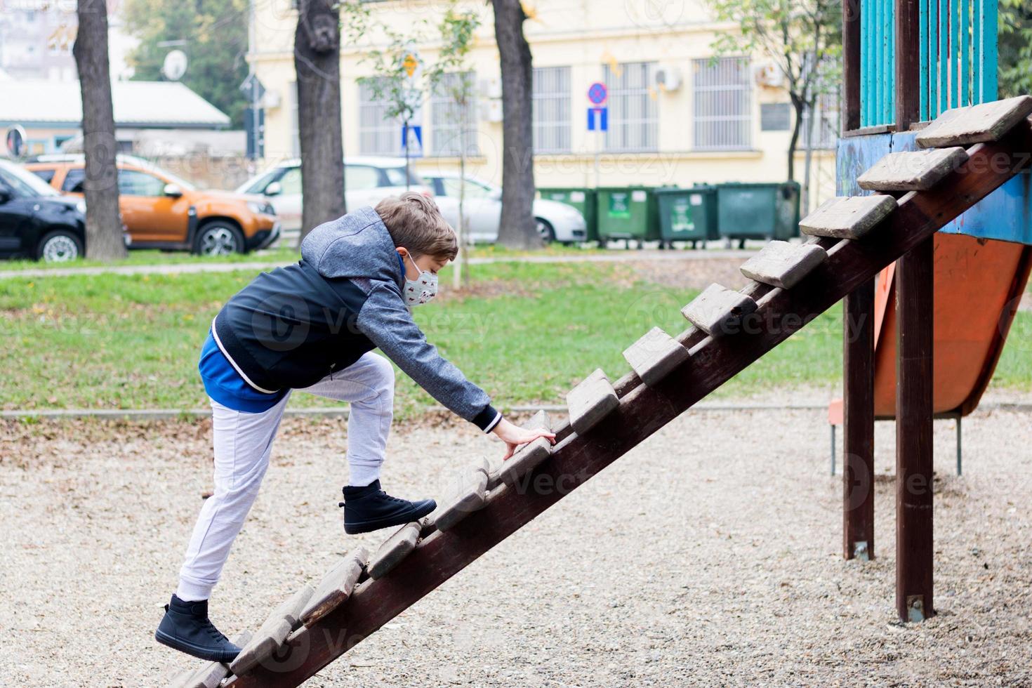 Kid playing o playground and wears face mask due to COVID-19 pandemic. photo