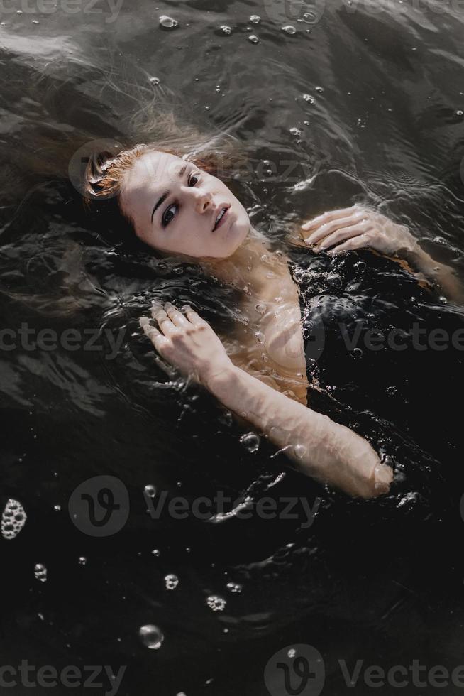 Young woman with raised arms in the water. Black water photo