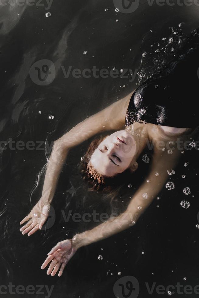 Young woman with raised arms in the water. Black water photo