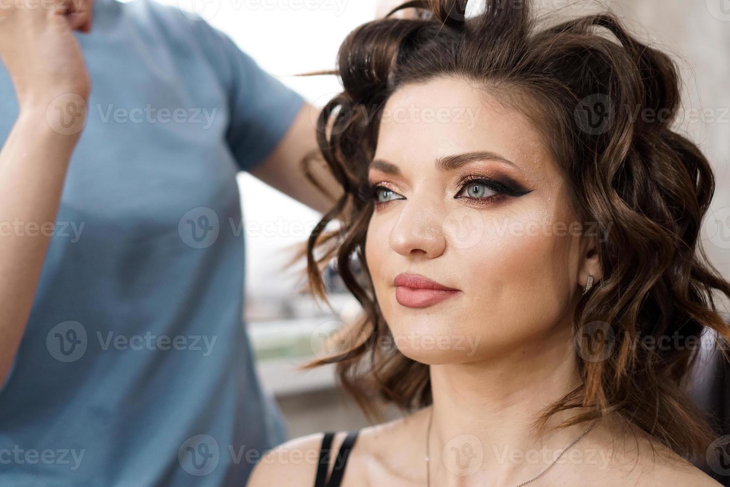 The hairdresser makes a hairstyle with curls to a beautiful brunette photo