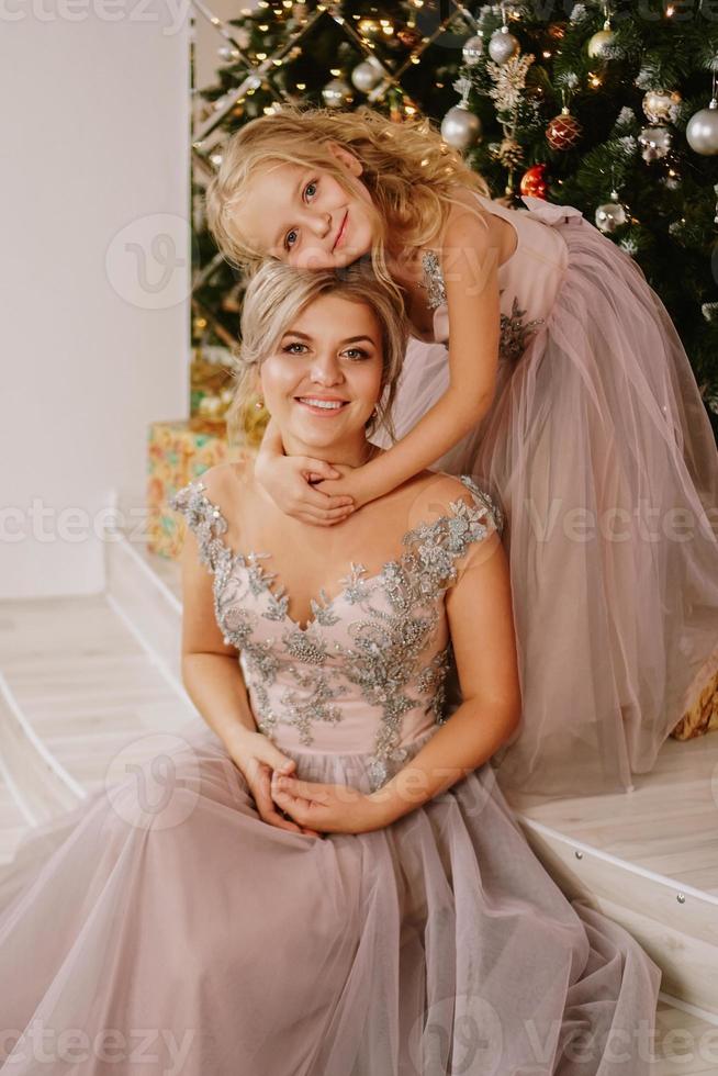 hija abrazando a su madre mientras está sentada en el árbol de navidad foto