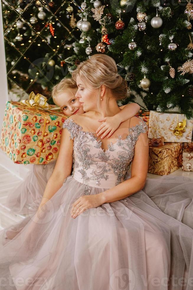 hija abrazando a su madre mientras está sentada en el árbol de navidad foto