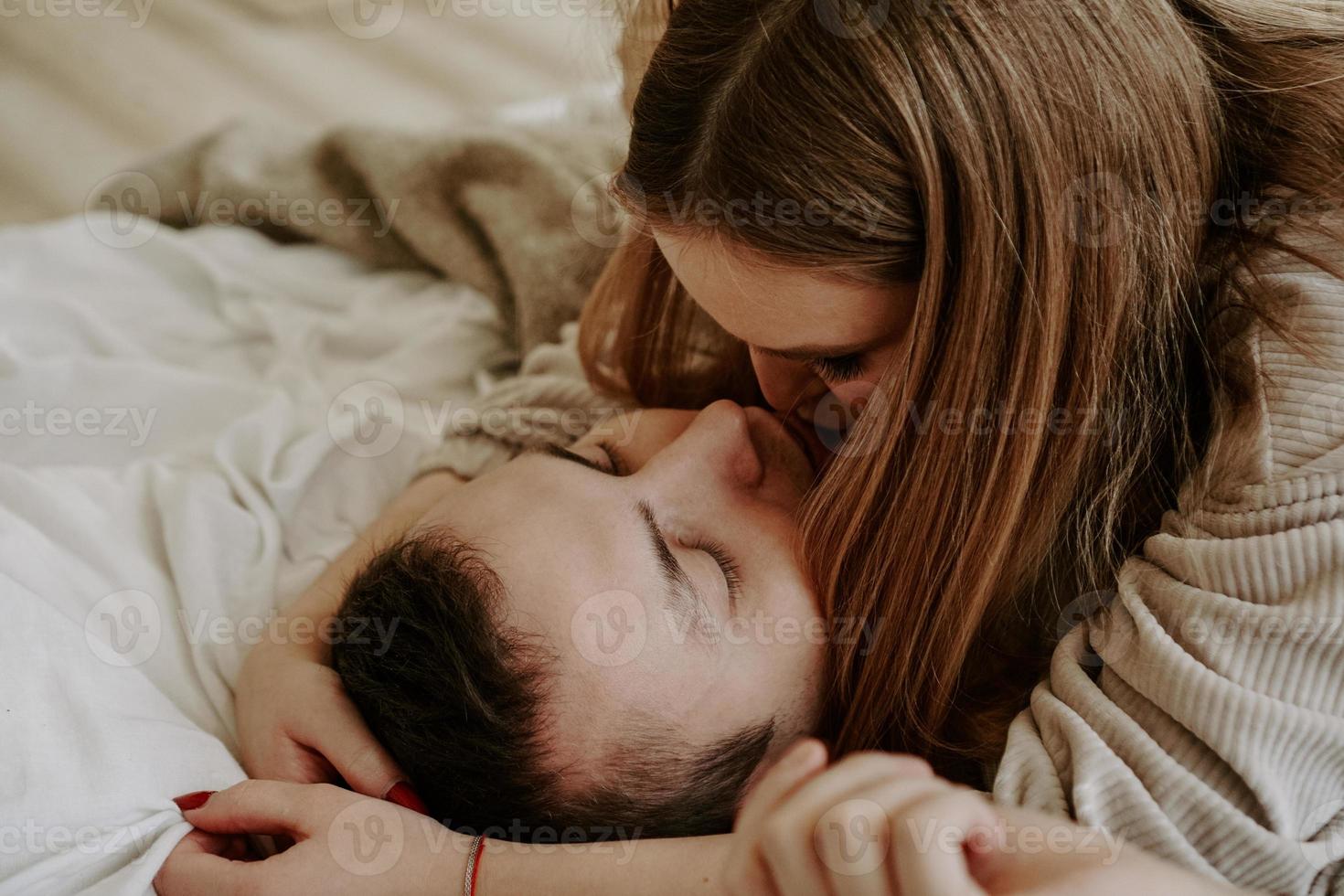 Close-up portrait of a beautiful young kissing couple in bed at home photo
