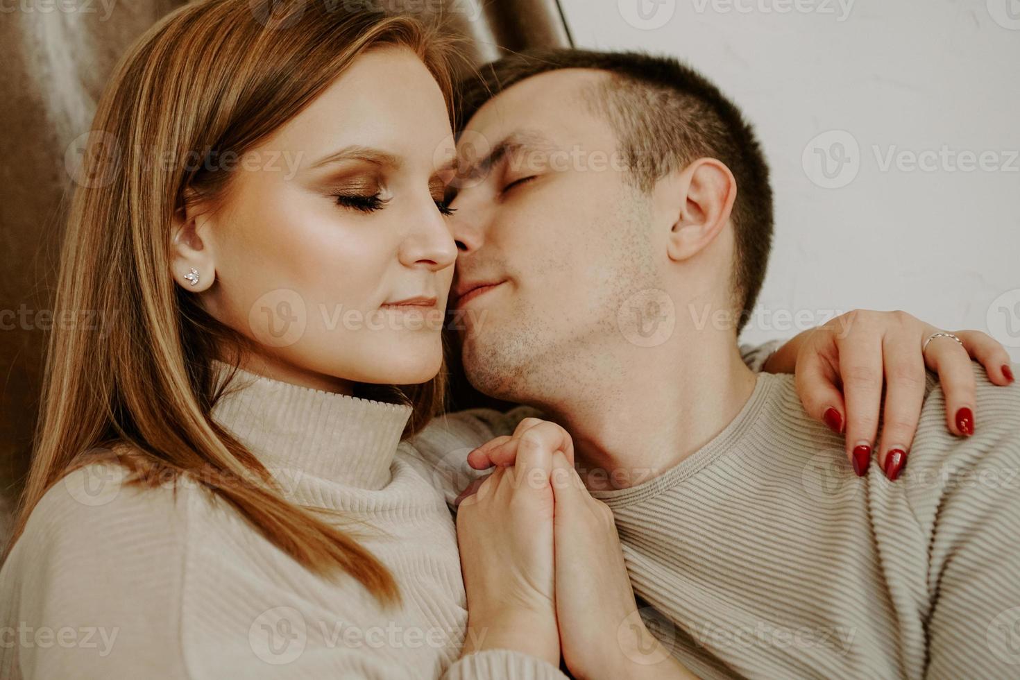 Close-up portrait of a beautiful young kissing couple in bed at home photo