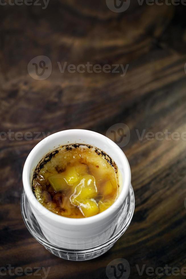 Tropical mango creme brulee dessert cup on wooden table photo