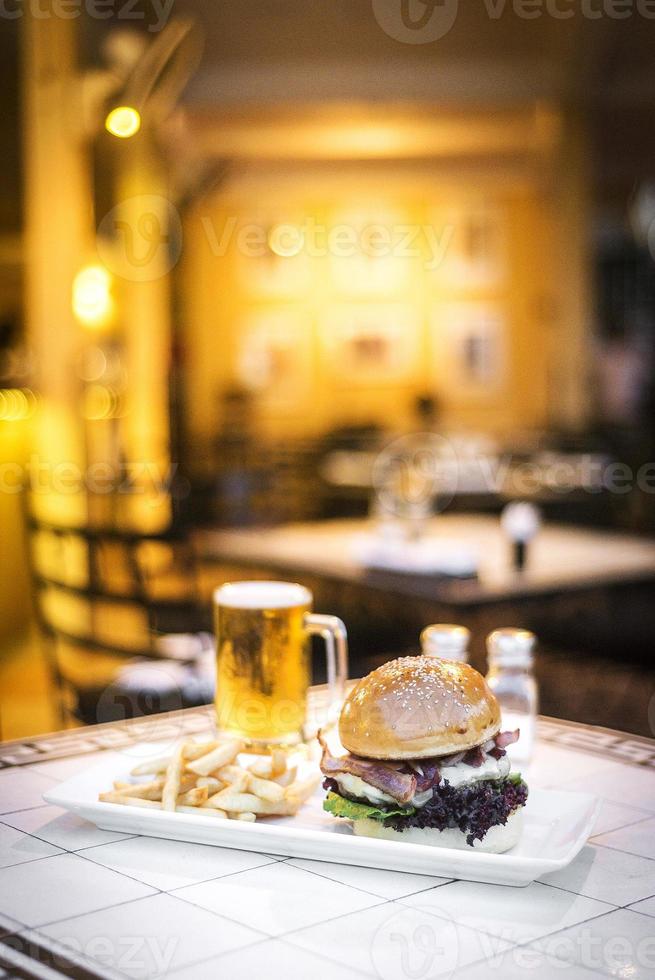 Hamburguesa de ternera gourmet con queso y tocino con papas fritas y cerveza de barril en una mesa de restaurante foto