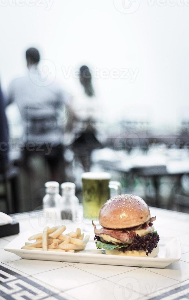 Hamburguesa de ternera gourmet con queso y tocino con papas fritas y cerveza de barril en una mesa de restaurante foto