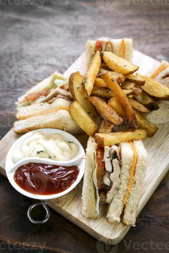 Sándwich club gourmet clásico con papas fritas sobre tabla de madera foto