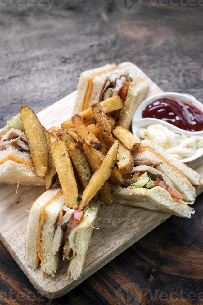 Sándwich club gourmet clásico con papas fritas sobre tabla de madera foto