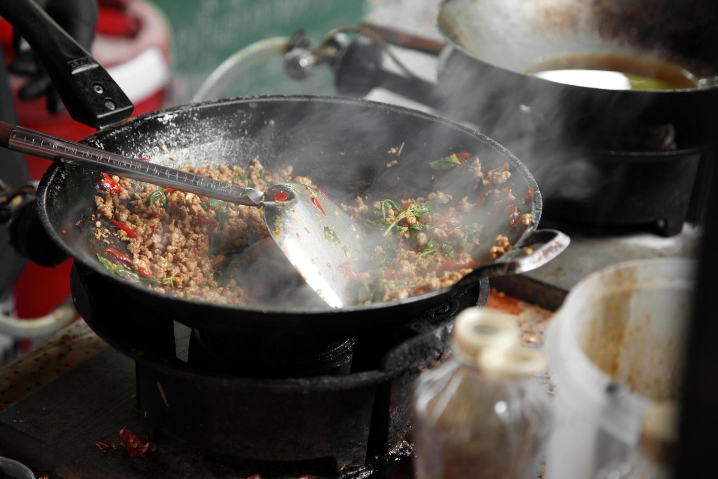 Cocinar carne de cerdo picada salteada tailandesa con albahaca en la sartén de metal foto