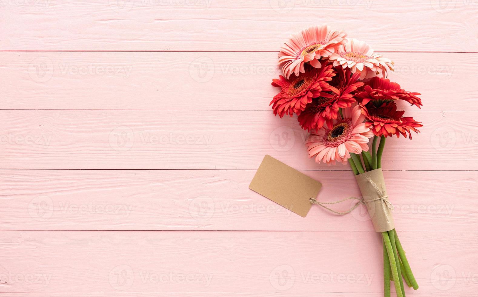 Red gerbera daisy flowers and blank craft label tag on pink photo