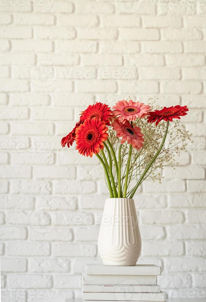 Margaritas gerberas brillantes en jarrón blanco sobre una pila de libros blancos foto