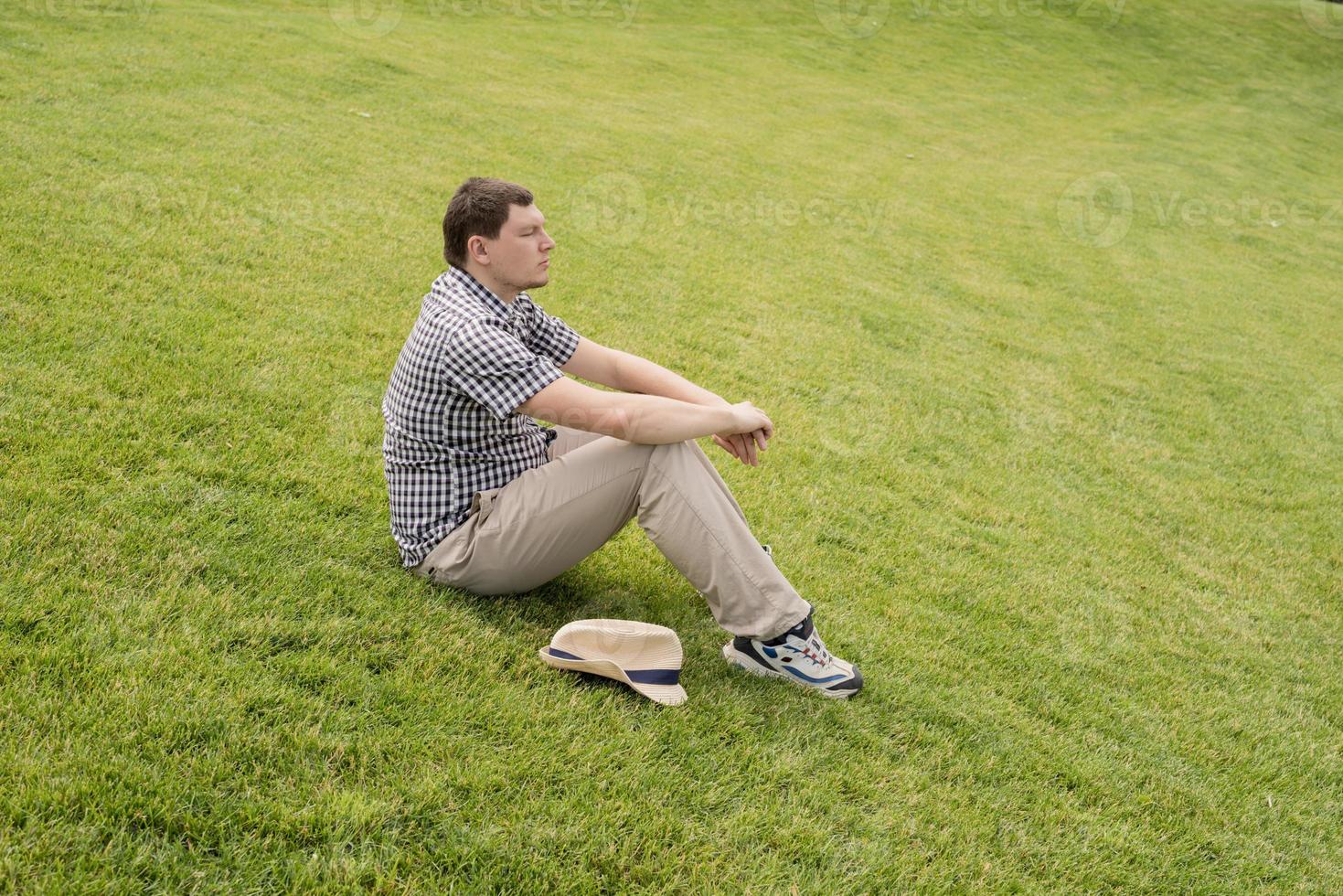 Young thoughtful man sitting on the grass in the park photo