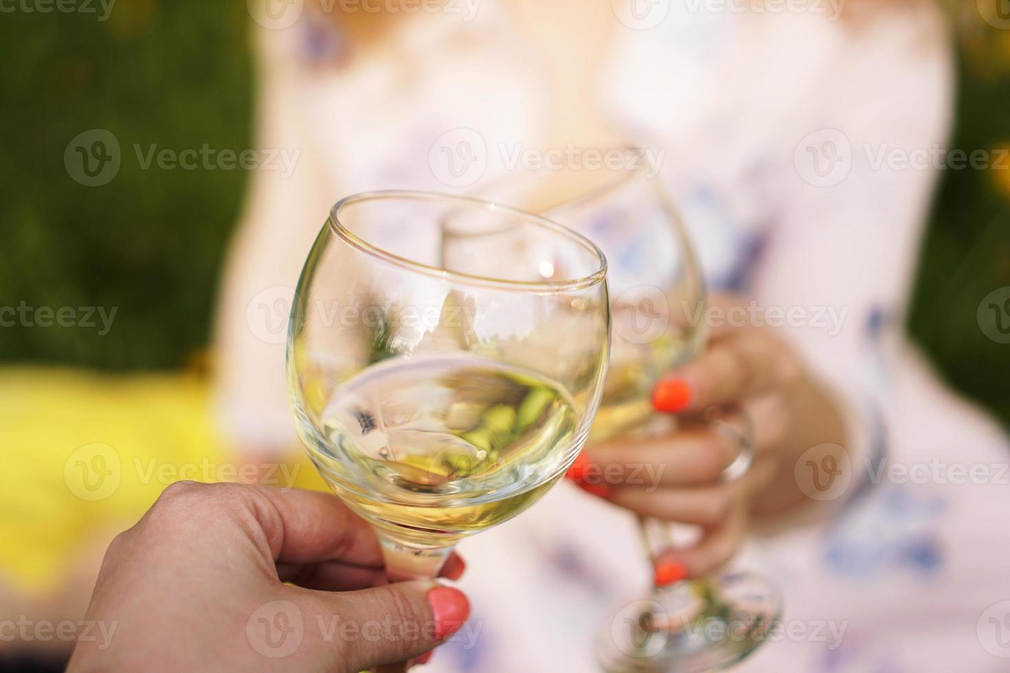 Las mujeres tintinean vasos con vino sabroso sobre fondo claro foto