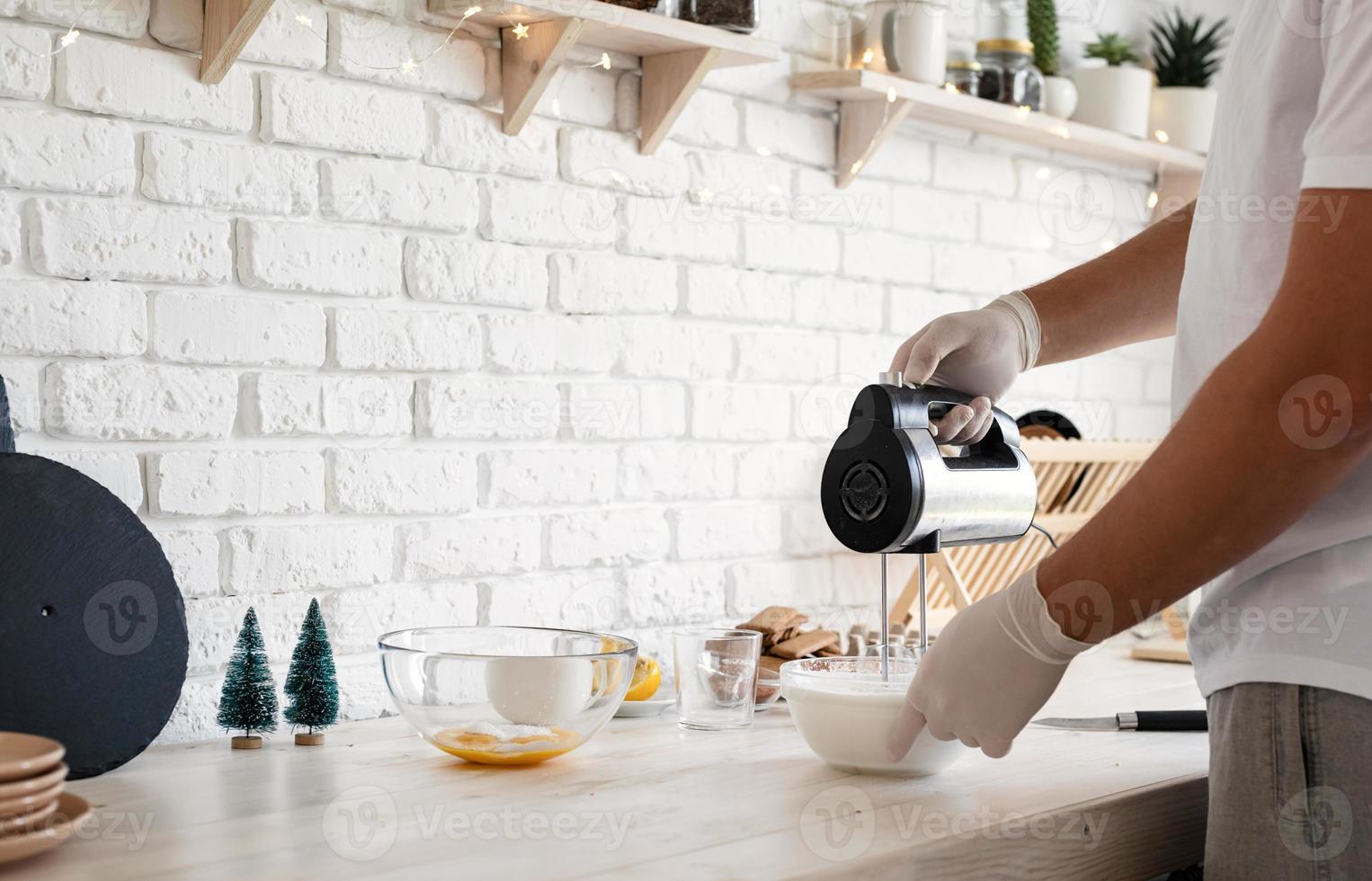 Man in gloves whipping egg whites with the electric mixer photo