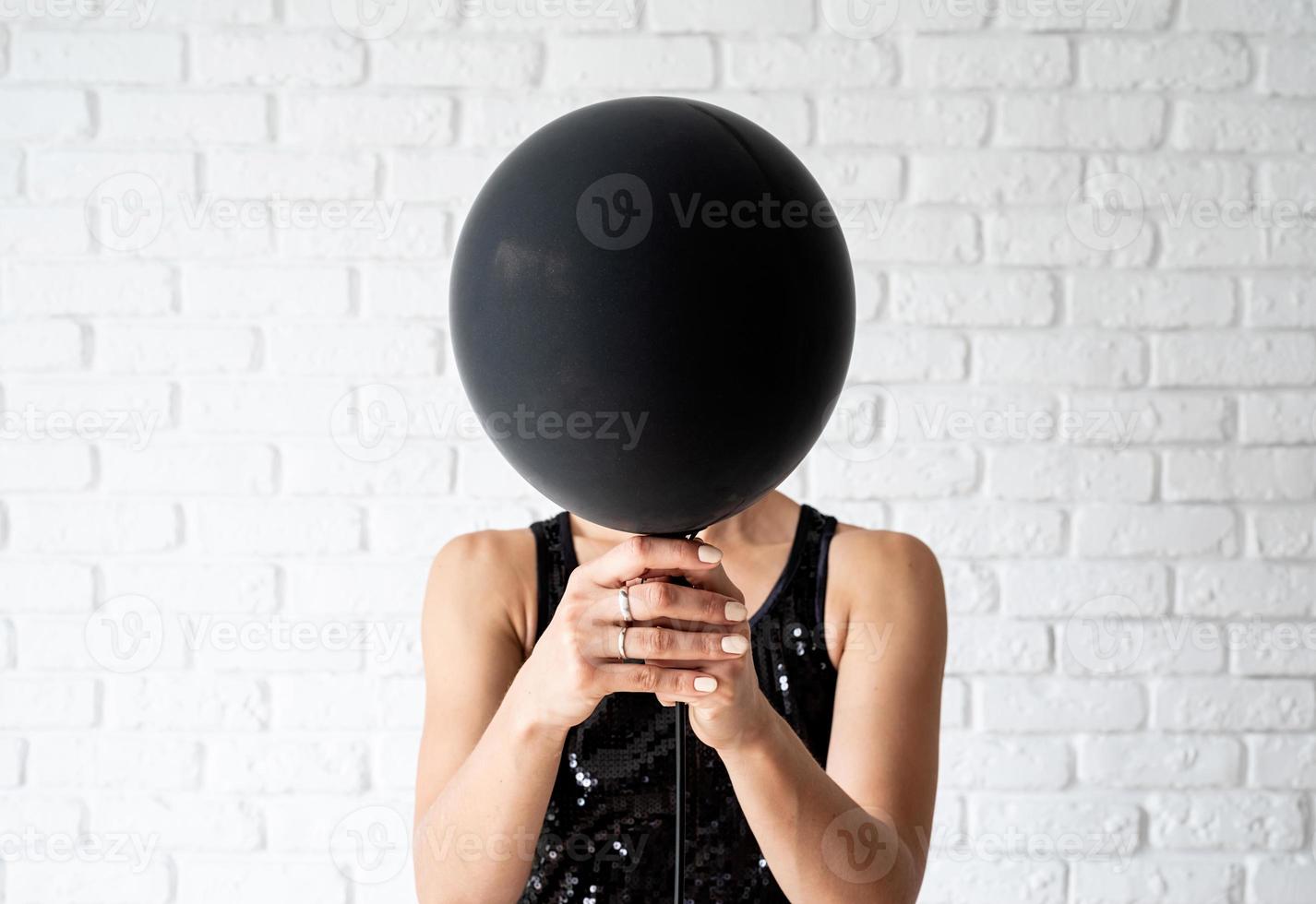 Woman in black dress holding black balloon in front of her face photo