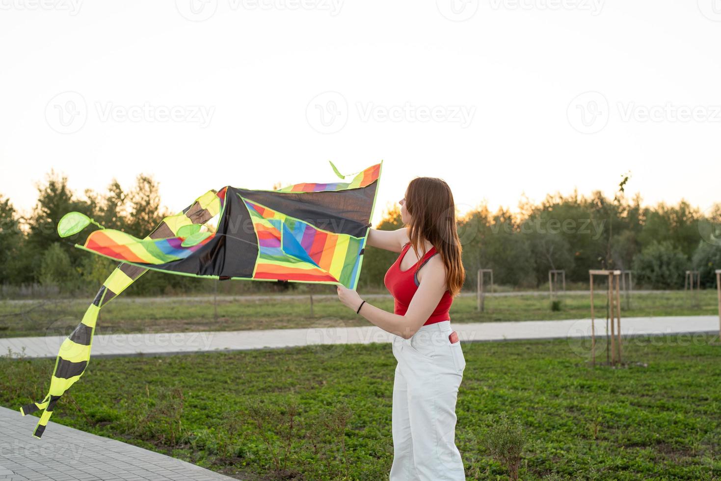 Mujer joven volando una cometa en un parque público al atardecer foto