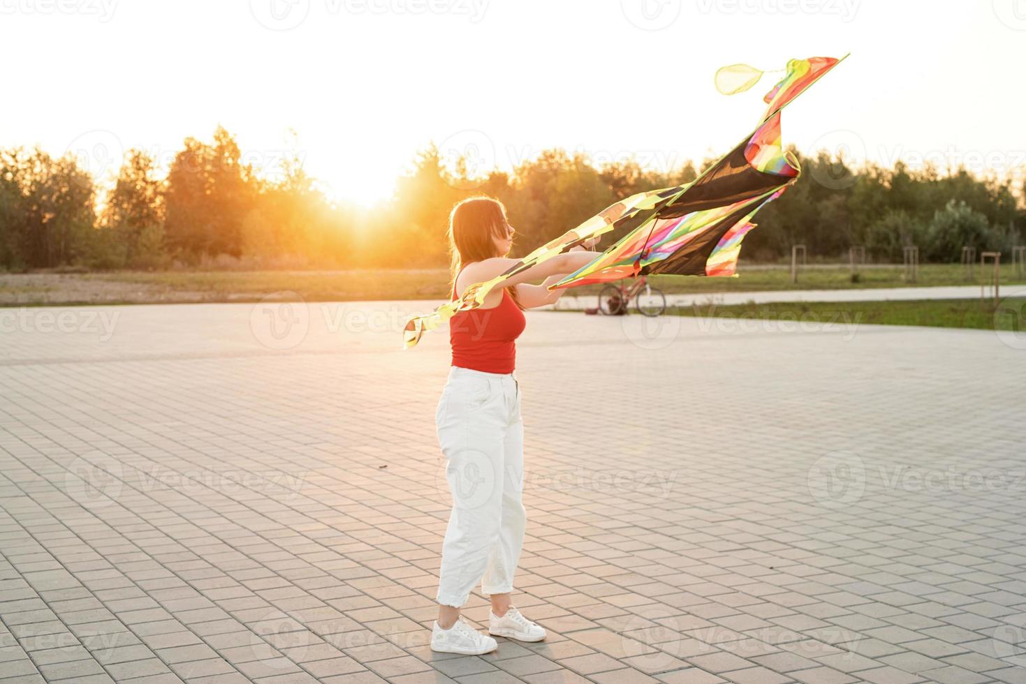 Mujer joven volando una cometa en un parque público al atardecer foto