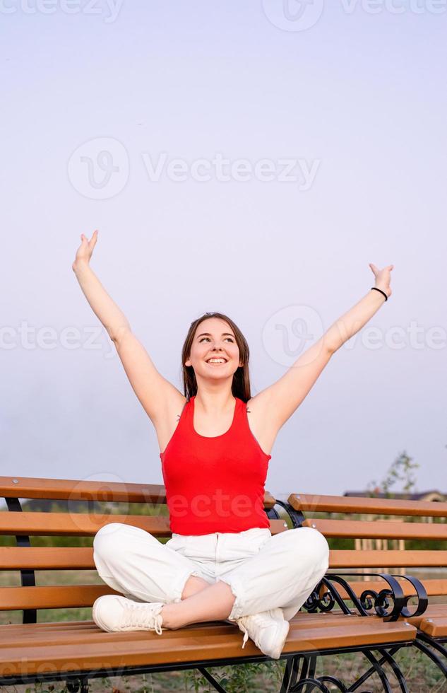 feliz, mujer joven, sentado, en, un, banco, con, piernas cruzadas foto