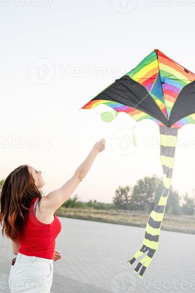 Mujer joven volando una cometa en un parque público al atardecer foto