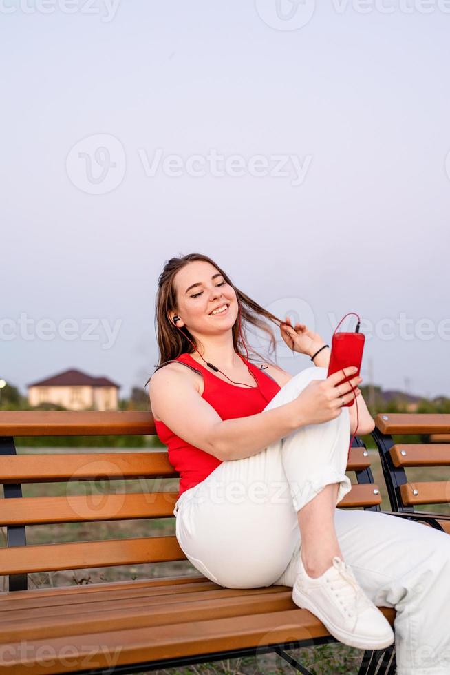 Feliz joven adolescente sentada en un banco en el parque escuchando foto
