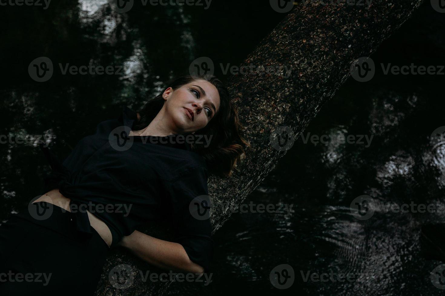 Mujer vestida de negro sobre un fondo de agua, se encuentra en un árbol foto