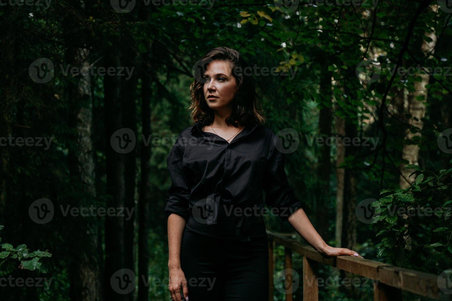 Young woman - close portrait in a dark forest. Woman in black shirt photo