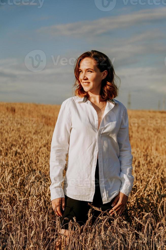 mujer joven feliz con una camisa blanca en un campo de trigo. día soleado. foto