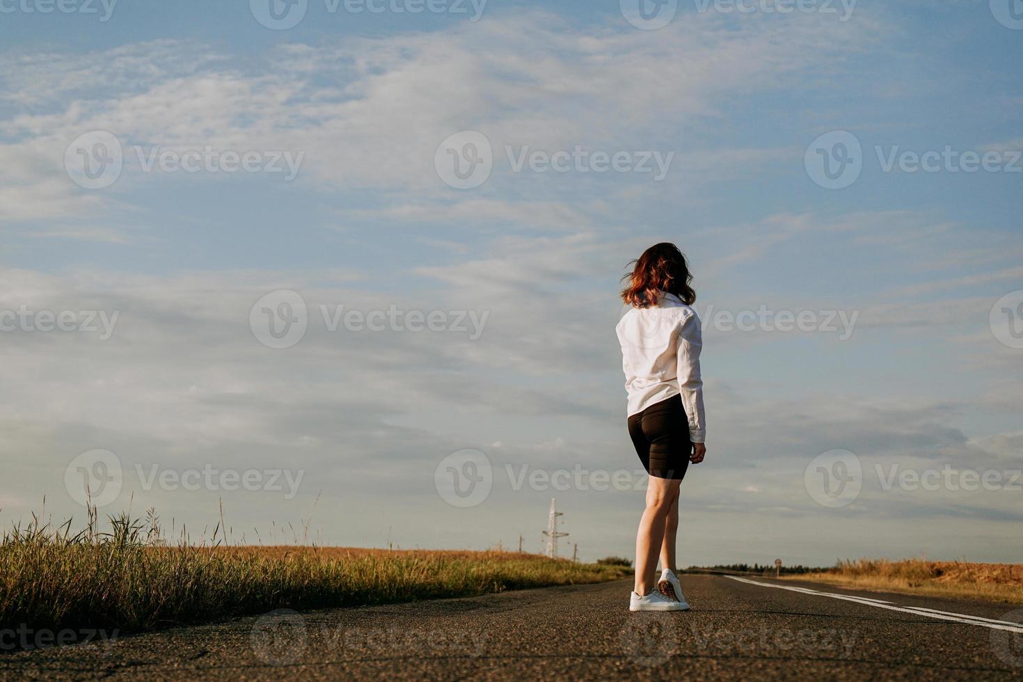 Woman in a white shirt walks along the road among the fields photo