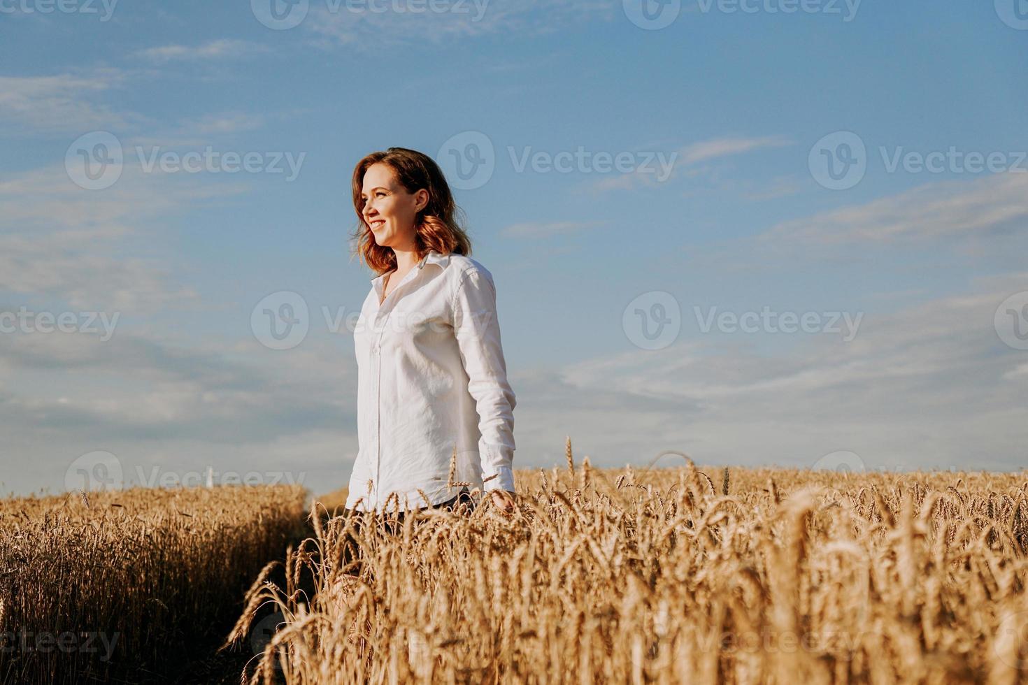 Happy young woman in a white shirt in a wheat field. Sunny day. photo