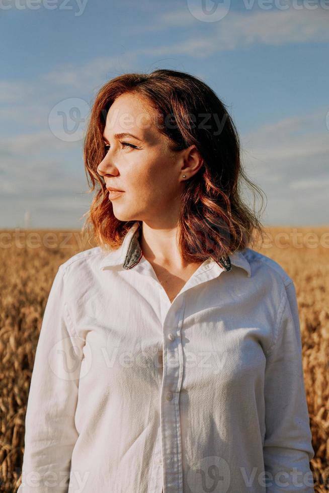 chica pelirroja con una camisa blanca. ella en el campo de centeno en un día soleado foto