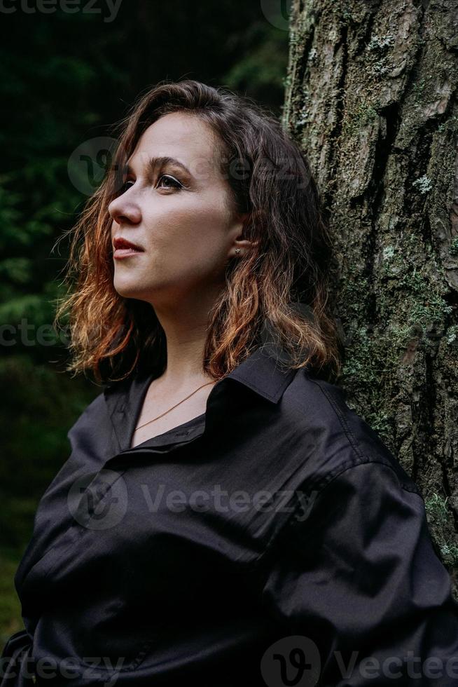 mujer joven - retrato cercano en un bosque oscuro. mujer en camisa negra foto